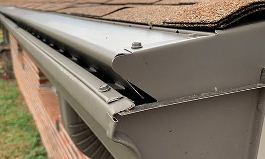 Hooded gutter guard installed along a shingle roofline